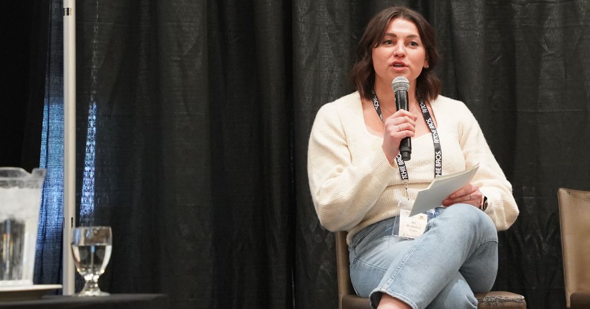 INDIGENOUS SUMMIT - AGRIBITION - CULTIVATOR - Bre Walkeden sits cross legged holding cuecards and microphone.