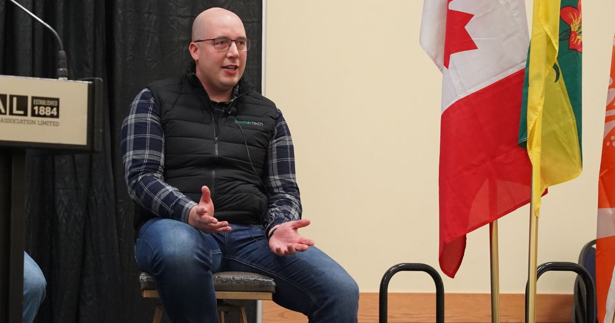 INDIGENOUS SUMMIT - Kyle Scott sits on a stage with Canadian flag and Saskatchewan flag beside him.