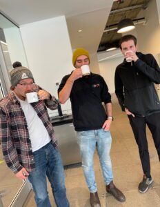 Three people stand in the Cultivator kitchen sipping their hot chocolate from their mugs.