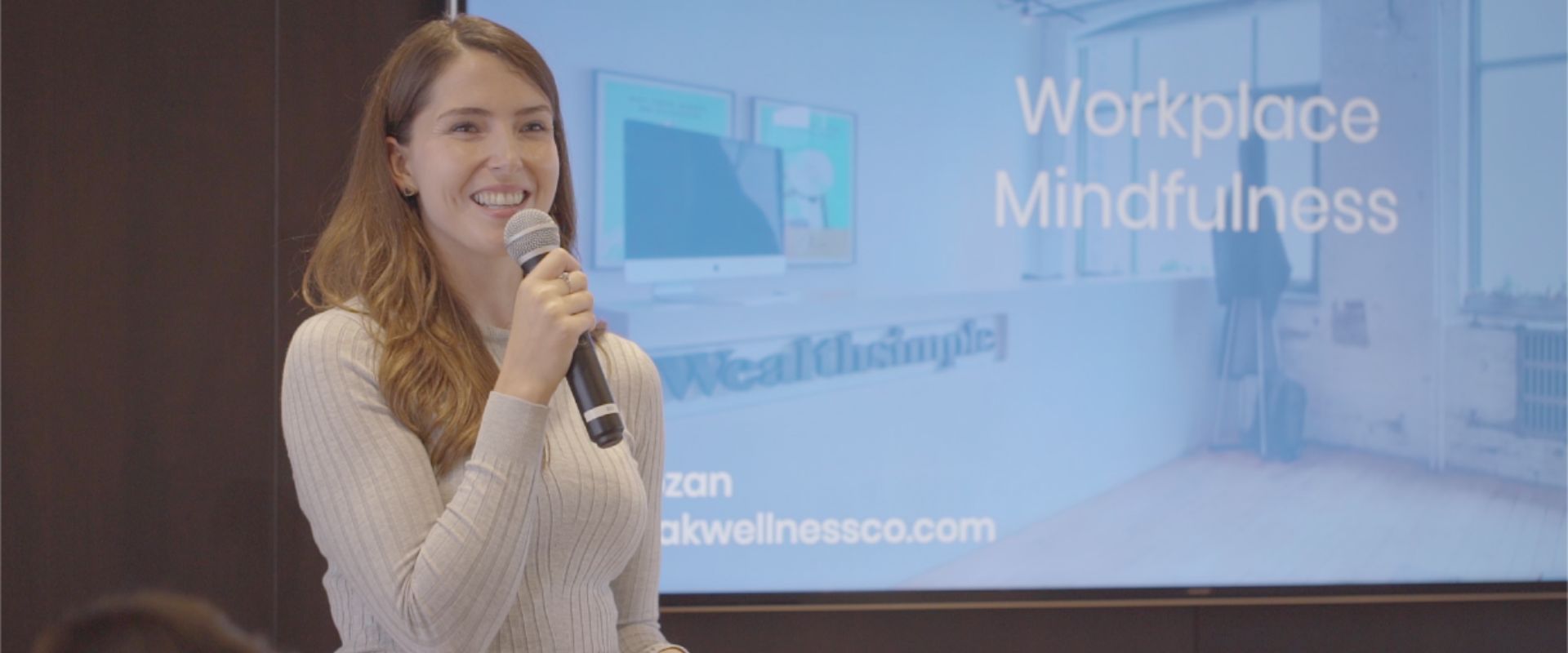 Twello CEO, Kayla Baum, holding a mic with a workplace mindfulness presentation slide behind her.