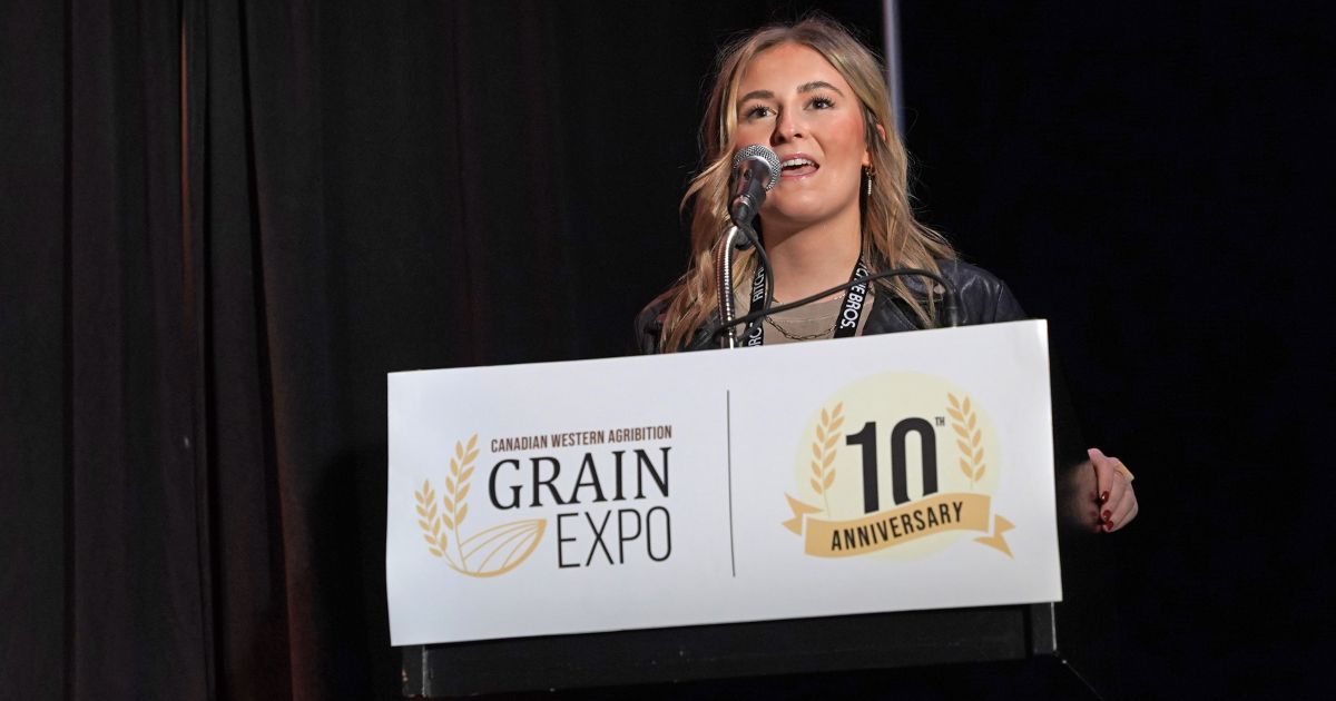 Breanne Dmytriw stands at Grain Expo podium speaking to audience.