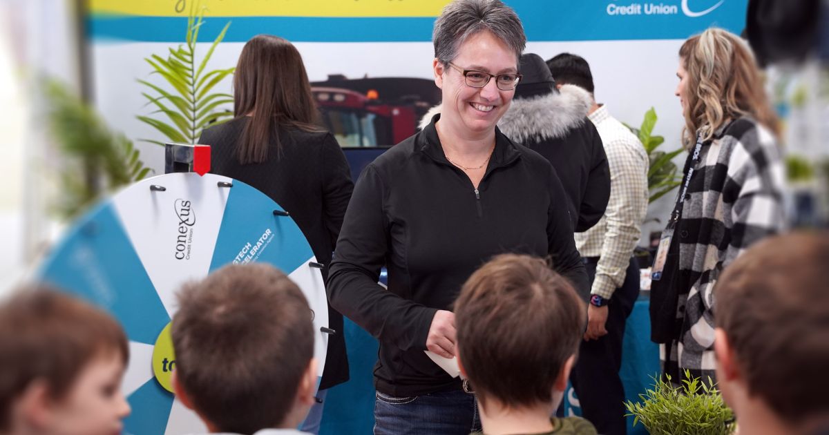 Conexus employee stands at the tradeshow booth smiling and talking to school aged children.