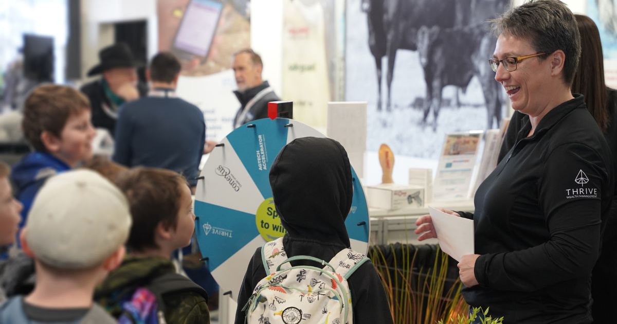 Conexus employee stands at the tradeshow booth smiling and talking to school aged children.