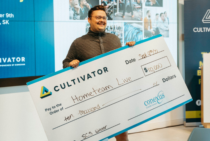 Tanner Goetz, founder of HomeTeam Live, smiling with $10,000 cheque