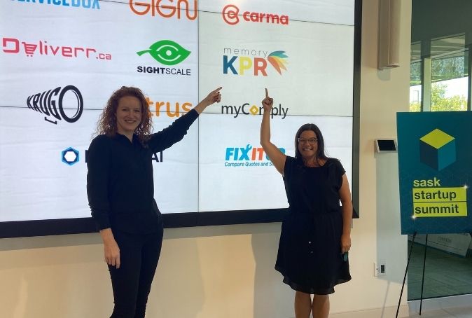 Photo of Taylor Fox and Jessica McNaughton smiling and pointing at picture of memoryKPR logo on big screen