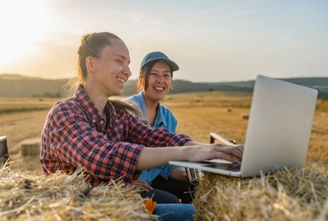 Two female ag producers sitting in field on computer