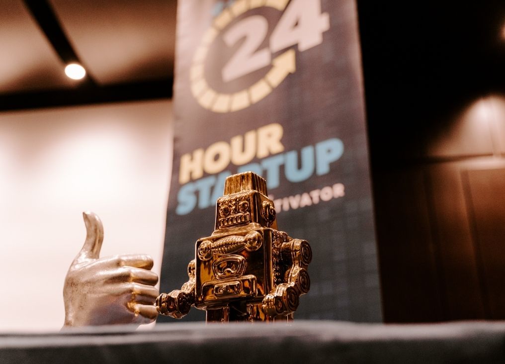 24 Hour Startup signage with robot and thumbs up statue in front