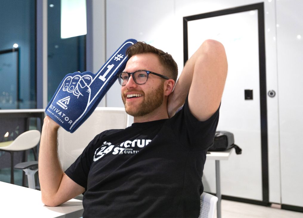 David Crossman holds a Cultivator foam finger up wearing a 24 Hour Startup shirt.