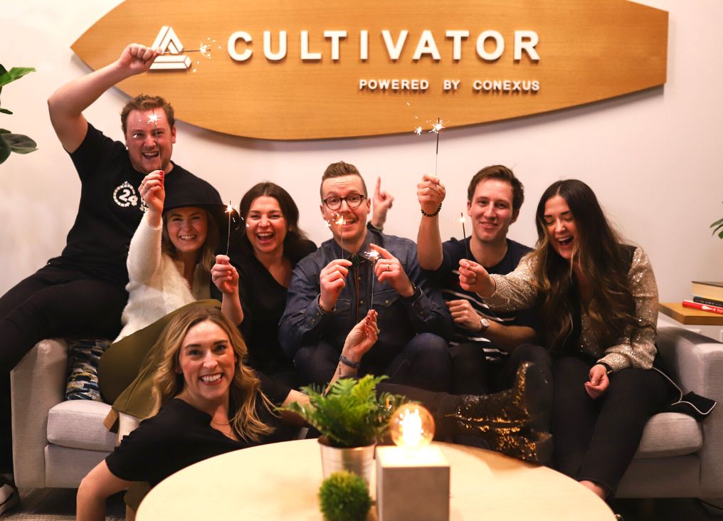 Group of people sit under a Cultivator sign holding sparklers.