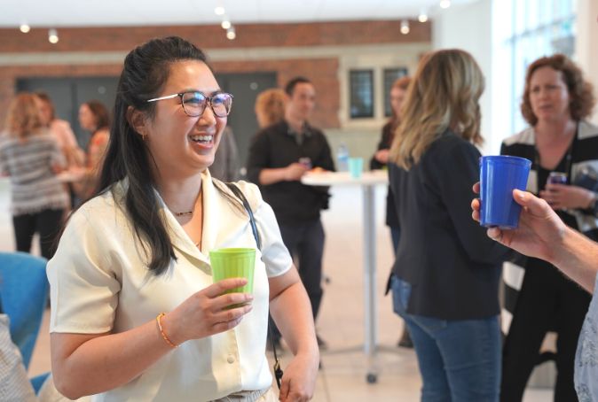 Annie Quangtakoune holds a green cup smiling talking to another person.