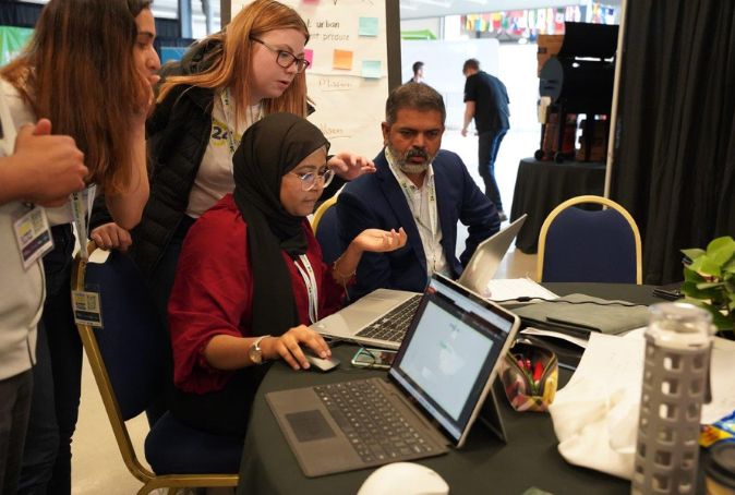 Four people surround a computer while collaborating on new innovation idea