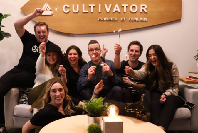 Group of people sit under a Cultivator sign holding sparklers.